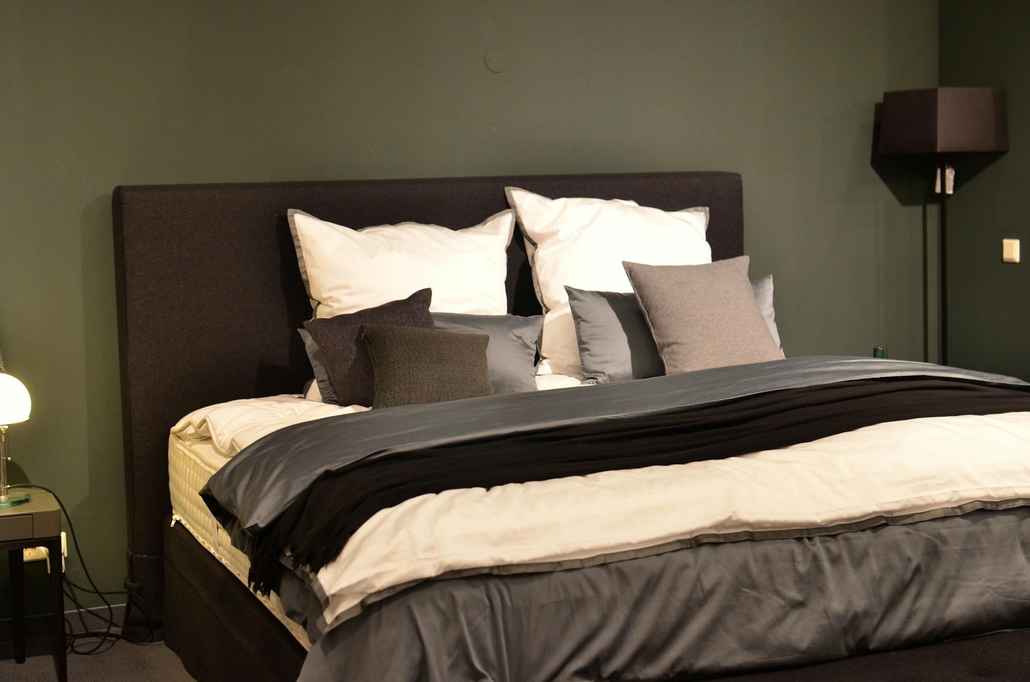 A modern bedroom with dark tones, featuring stylish bedding and a cozy atmosphere.