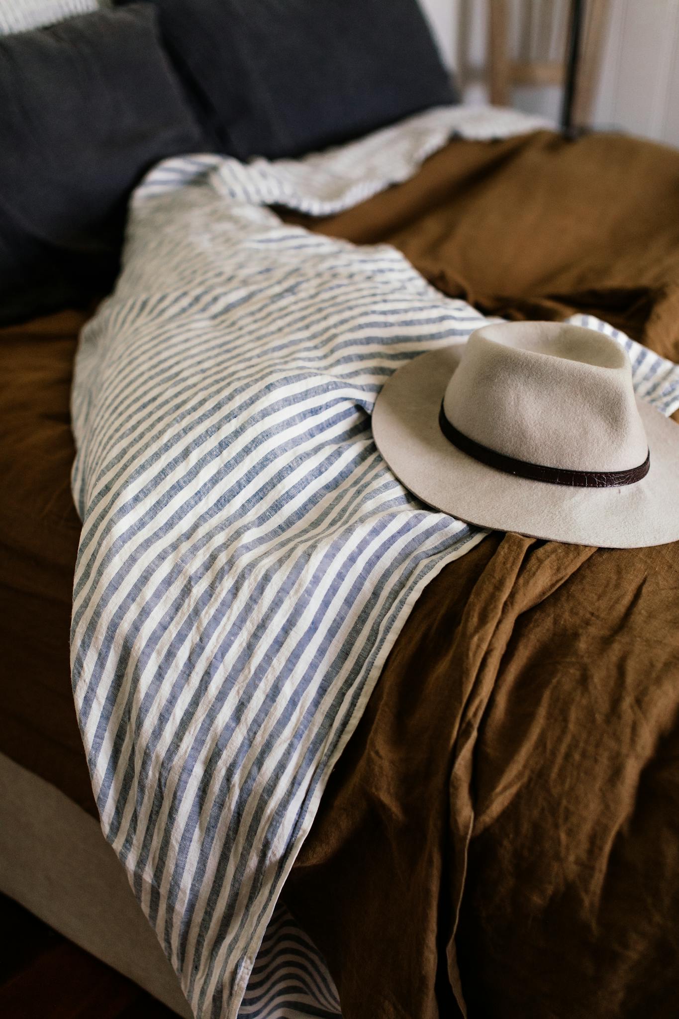 White stylish hat on blanket with stripes on unmade comfortable bed in bedroom